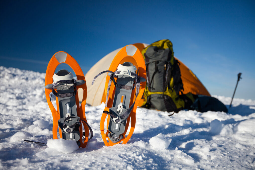 Orange snowshoes left in front of orange tent in winter